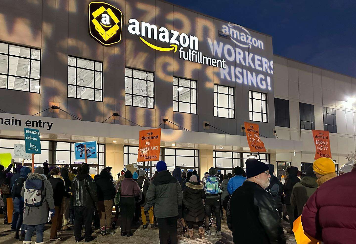 Outside huge warehouse supporters of Amazon Union rally in the snow at sundown