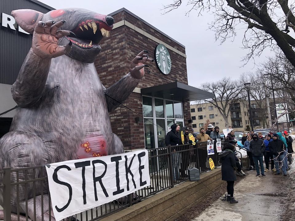 Larger than life rat puppet and crowd of strikers and supporters outside Cedar Ave Starbucks